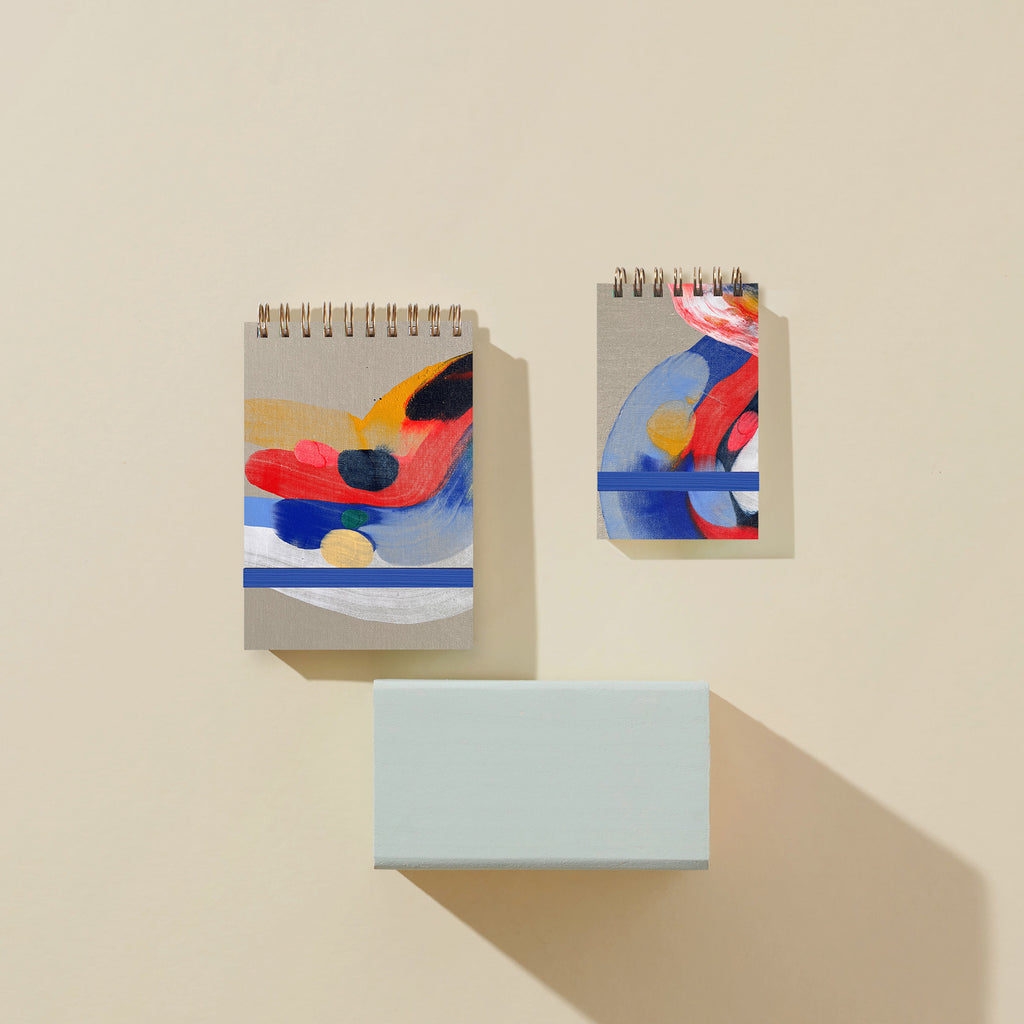 Two small spiral-bound notebooks with abstract designs on a beige background
