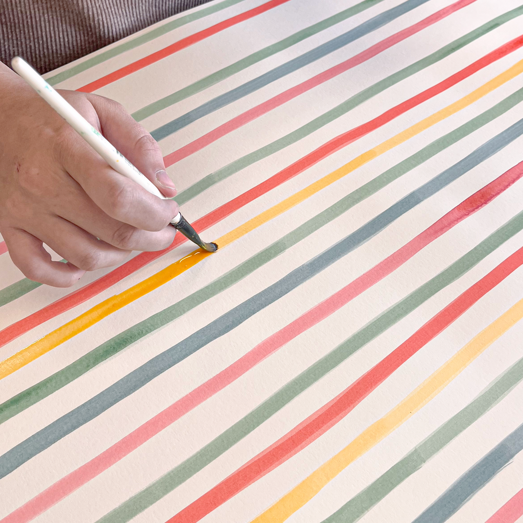 Person painting a striped surface with a container of paint.